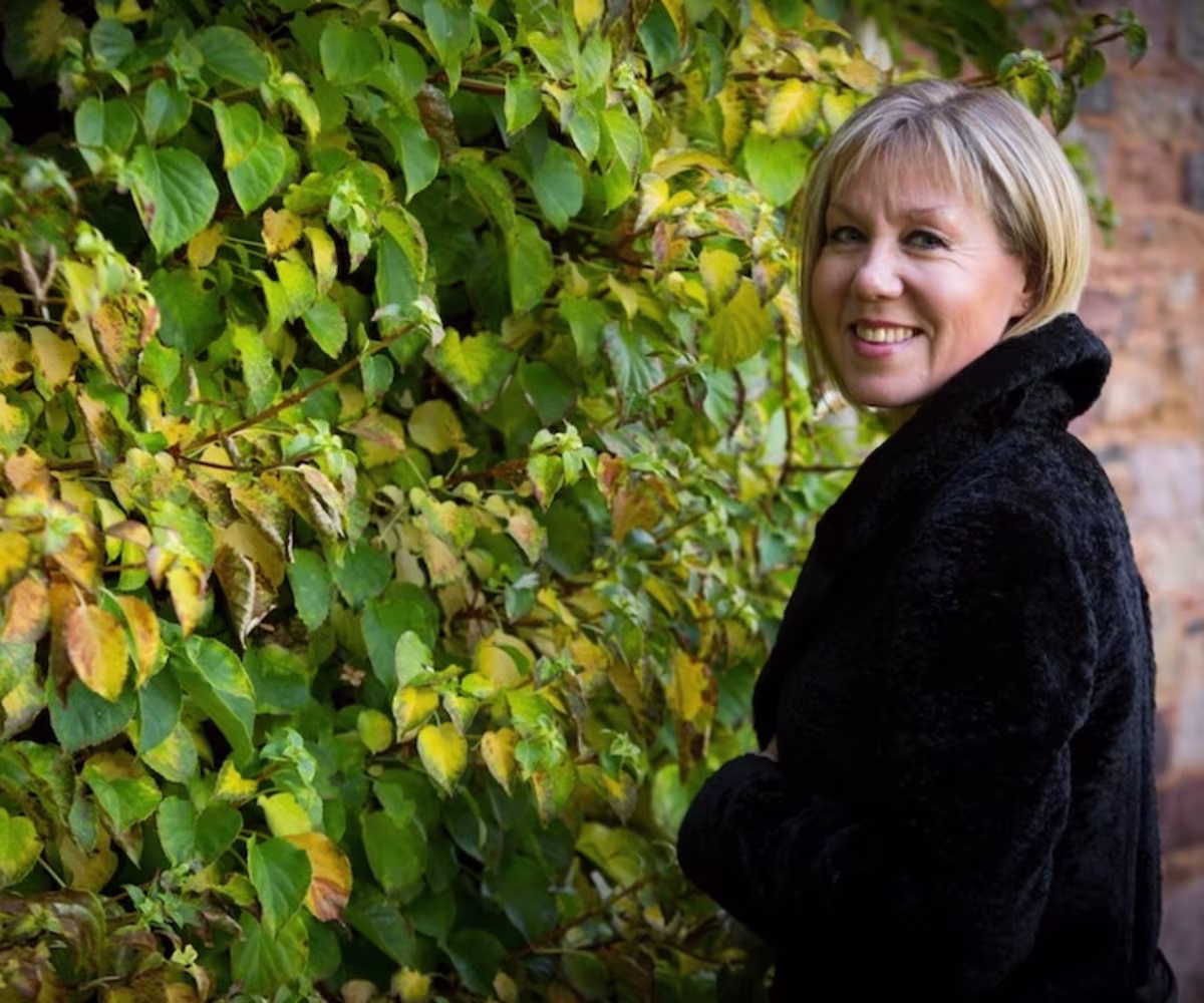 The Sounds and Songs of Auld Lang Syne soprano mhairi lawson wearing a black jacket standing inf ront of some gree climbing plants
