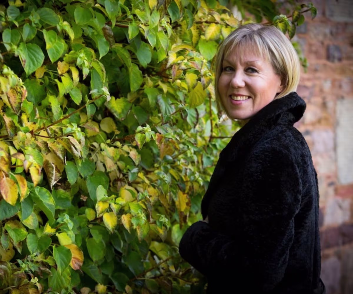 The Sounds and Songs of Auld Lang Syne soprano mhairi lawson wearing a black jacket standing inf ront of some gree climbing plants