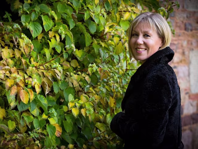The Sounds and Songs of Auld Lang Syne soprano mhairi lawson wearing a black jacket standing inf ront of some gree climbing plants
