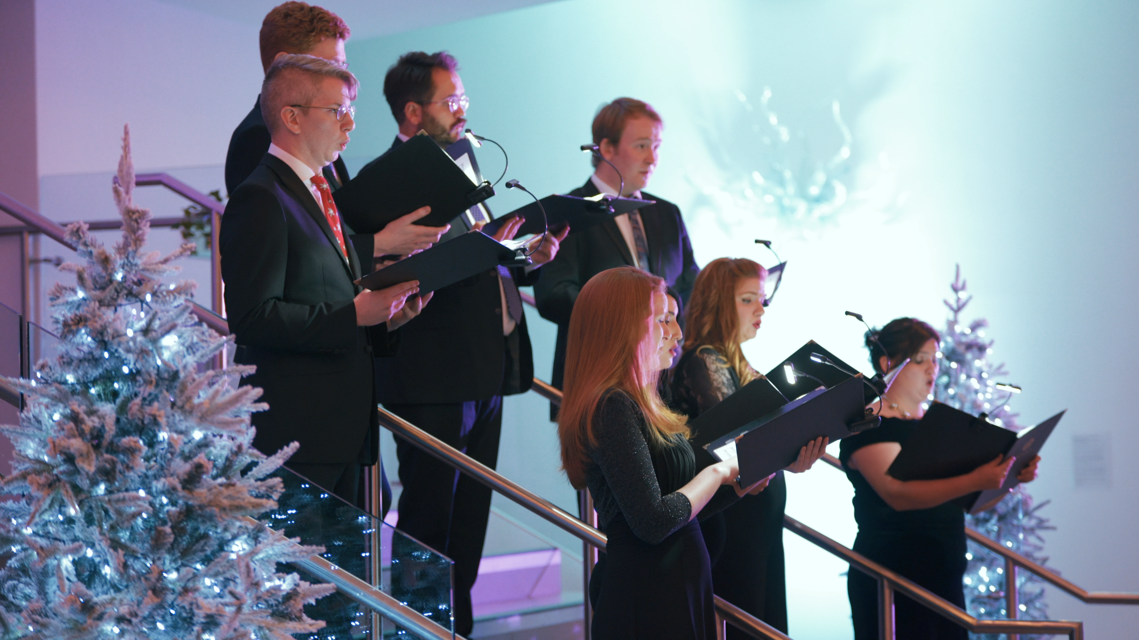 a choir of carol singers in a christmas setting with a snow covered christmas tree and lights