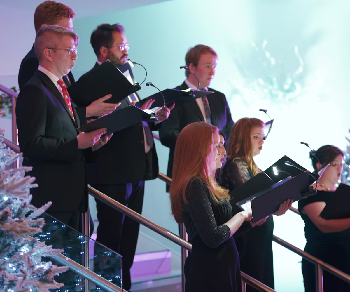 Carols at Christmas a choir of carol singers in a christmas setting with a snow covered christmas tree and lights