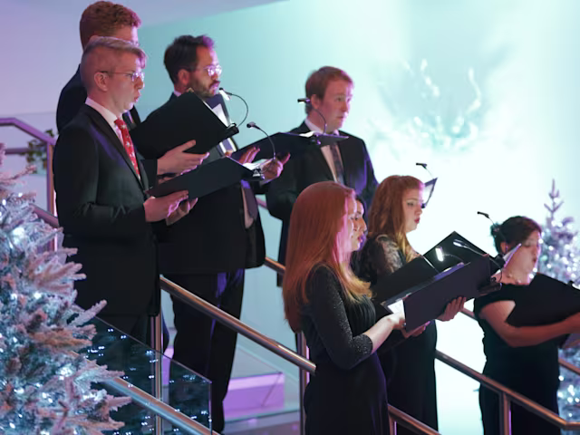 Carols at Christmas a choir of carol singers in a christmas setting with a snow covered christmas tree and lights