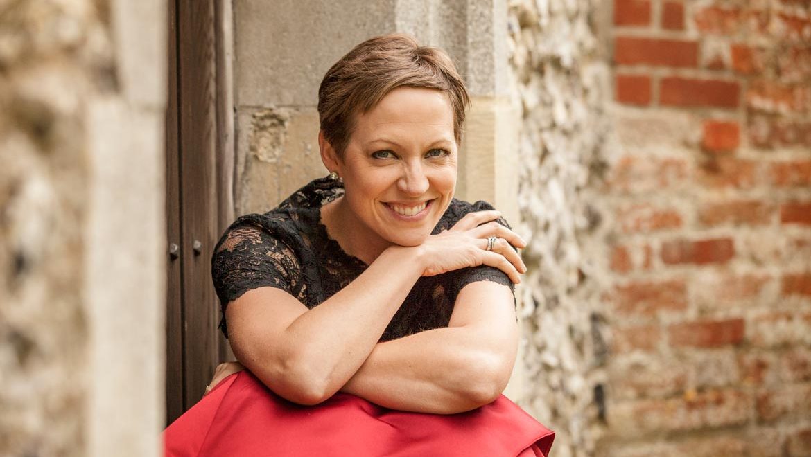 Soprano and Bach specialist Julia Doyle sitting on steps in red dress and black top. Photo by Louise O'Dwyer