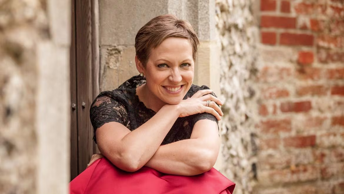 London Bach Society announces Study Day for singers Soprano and Bach specialist Julia Doyle sitting on steps in red dress and black top. Photo by Louise O'Dwyer