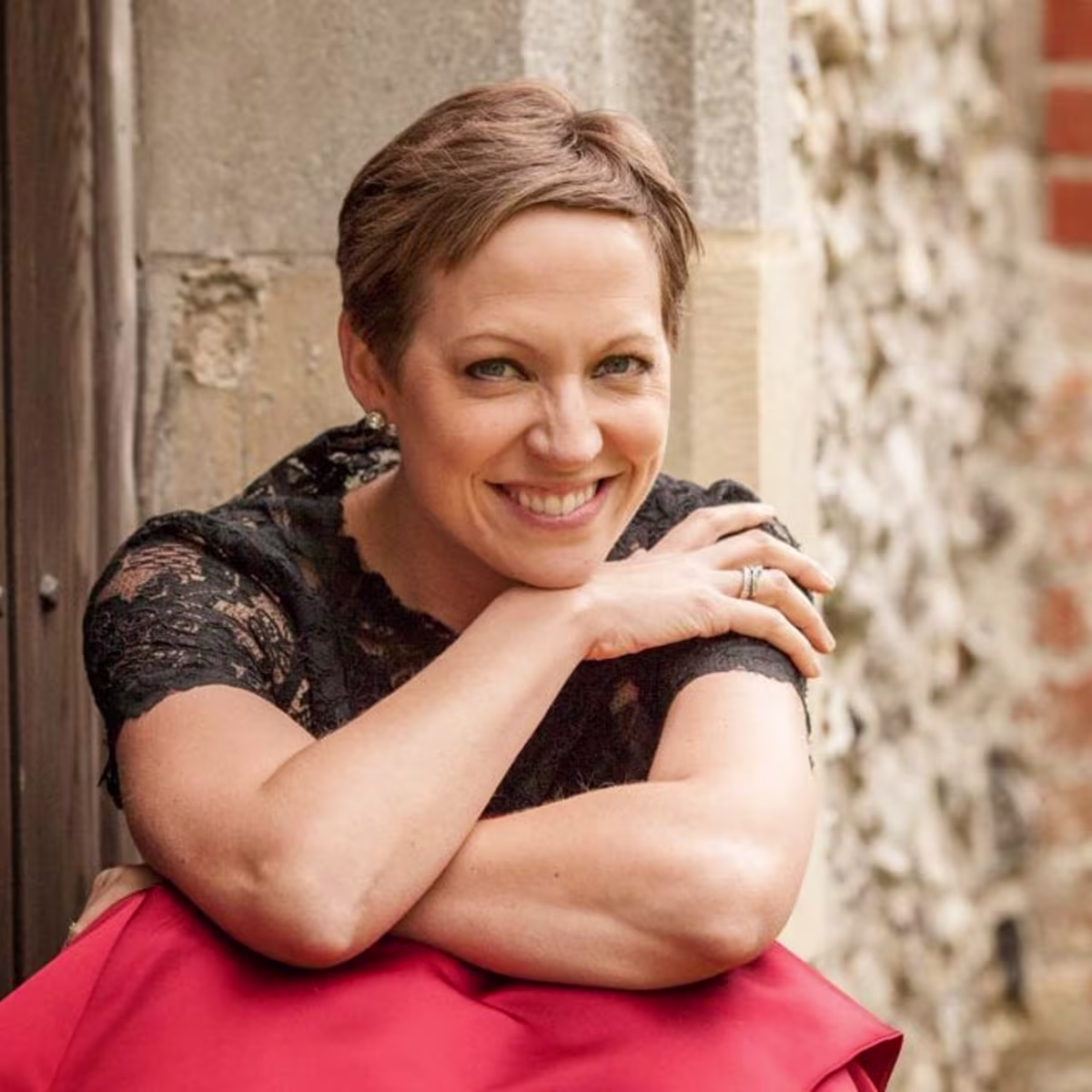 London Bach Society announces Study Day for singers Soprano and Bach specialist Julia Doyle sitting on steps in red dress and black top. Photo by Louise O'Dwyer