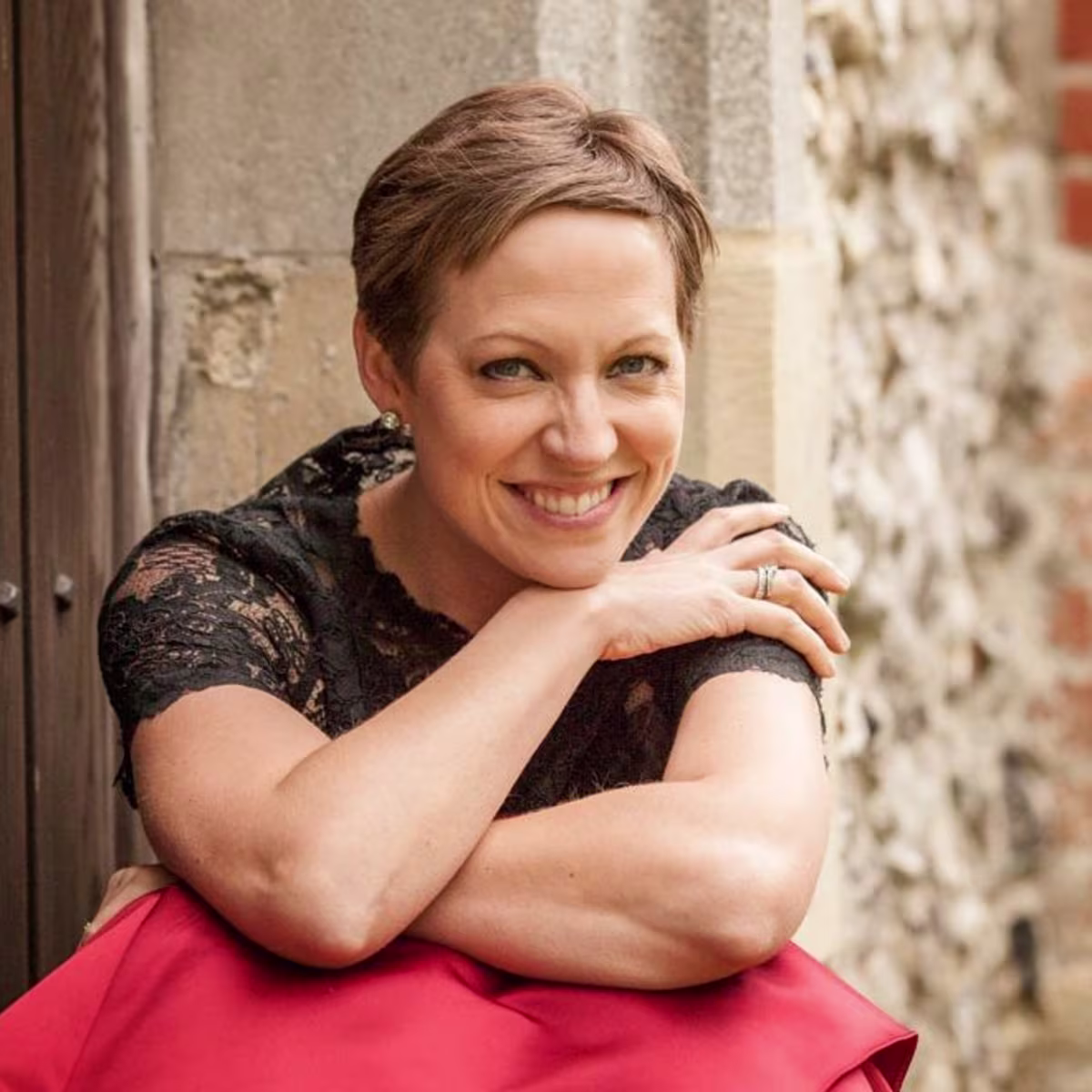 London Bach Society announces Study Day for singers Soprano and Bach specialist Julia Doyle sitting on steps in red dress and black top. Photo by Louise O'Dwyer