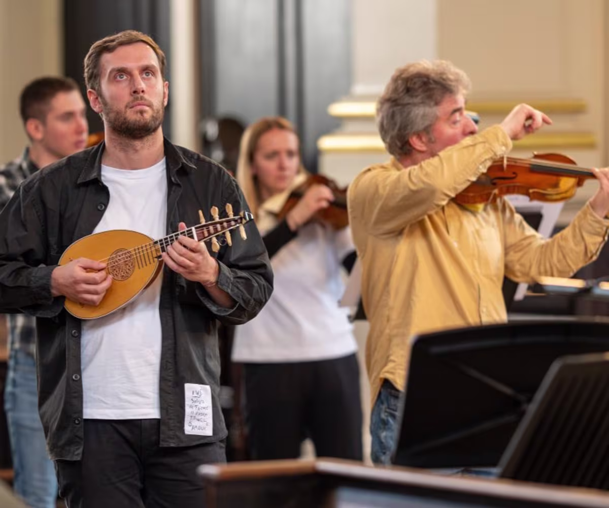 Vivaldi and Venice a man playing the mandolin standing up in front of a baroque orchestra