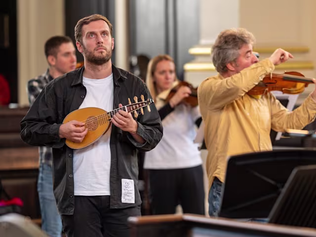 Vivaldi and Venice a man playing the mandolin standing up in front of a baroque orchestra