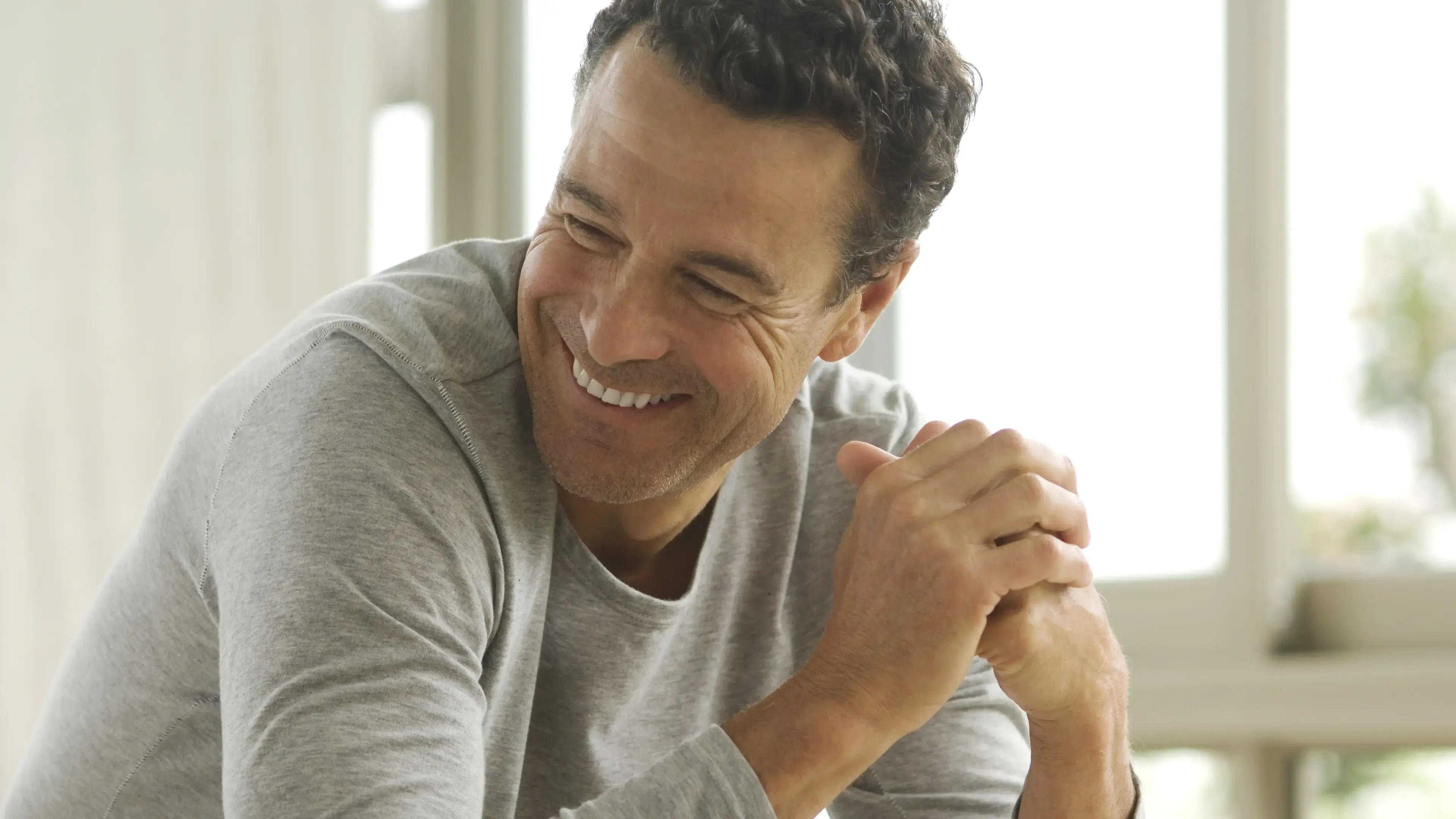 Ein lächelnder mann mittleren Alters, der seine Hände zusammen faltet.