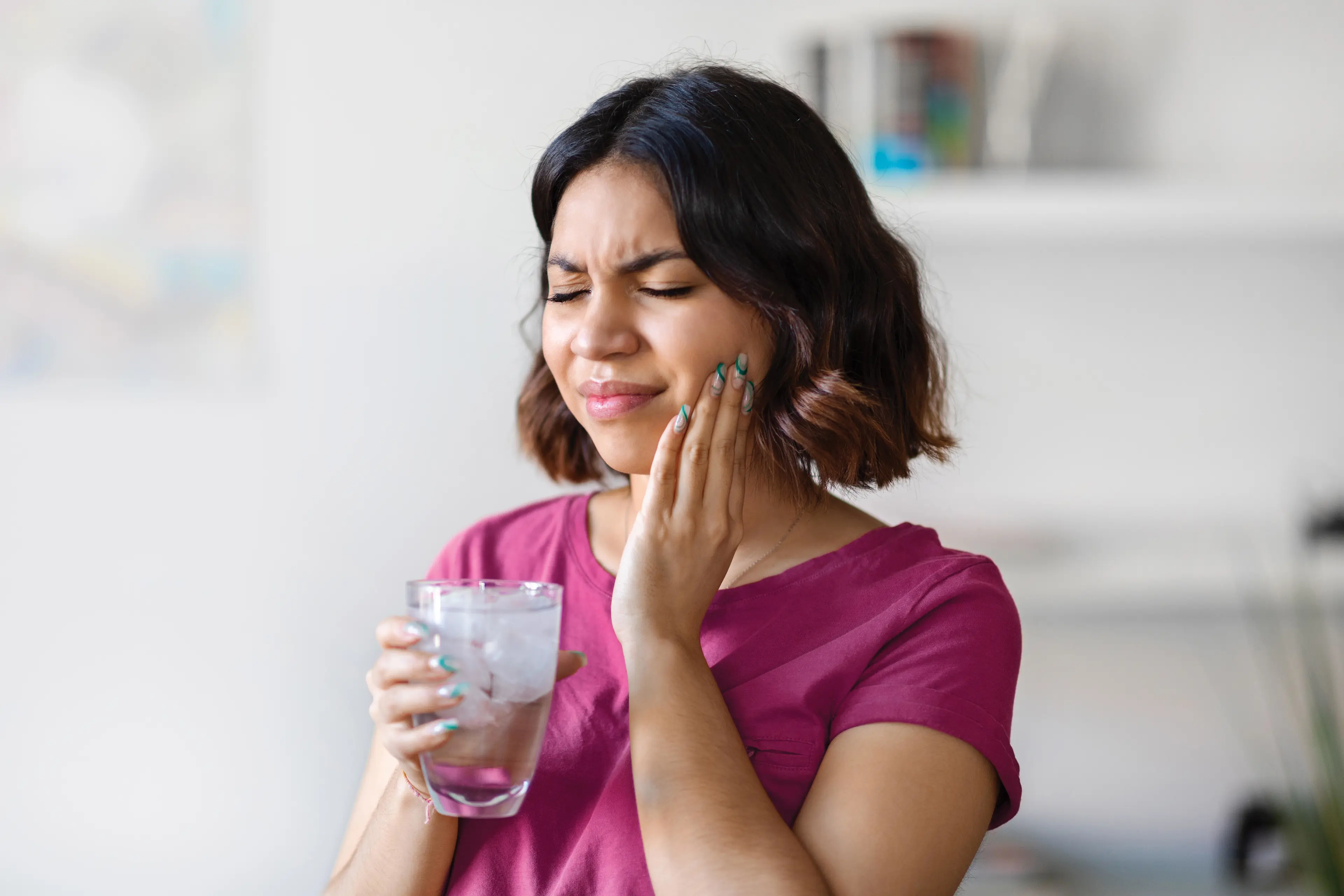 Eine Frau, die sich schmerzvoll an ihre linke Wange hält.