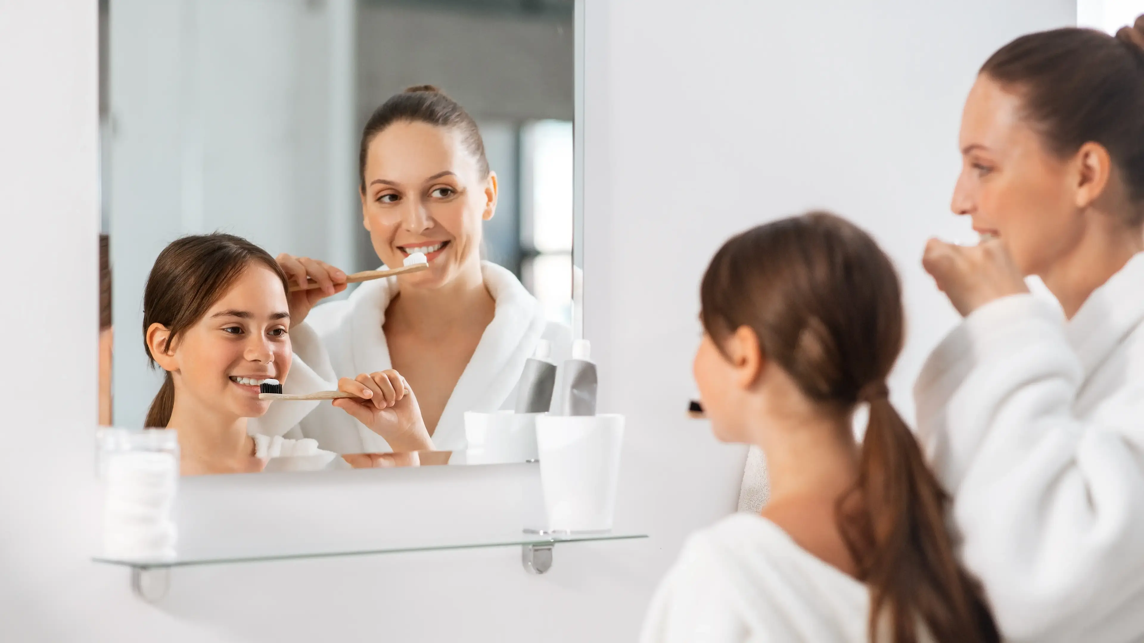 Eine Frau und Kind, die vor dem Badspiegel ihre Zähne putzen.