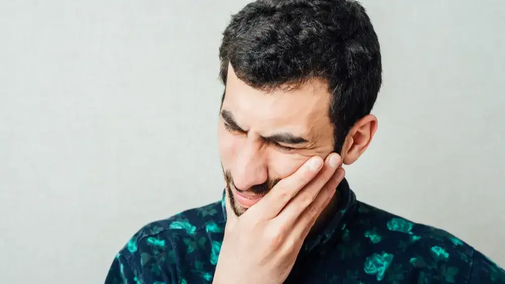 Ein Mann, dessen Gesicht schmerzverzehrt ist und sich die Hand an die linke Wange hält.