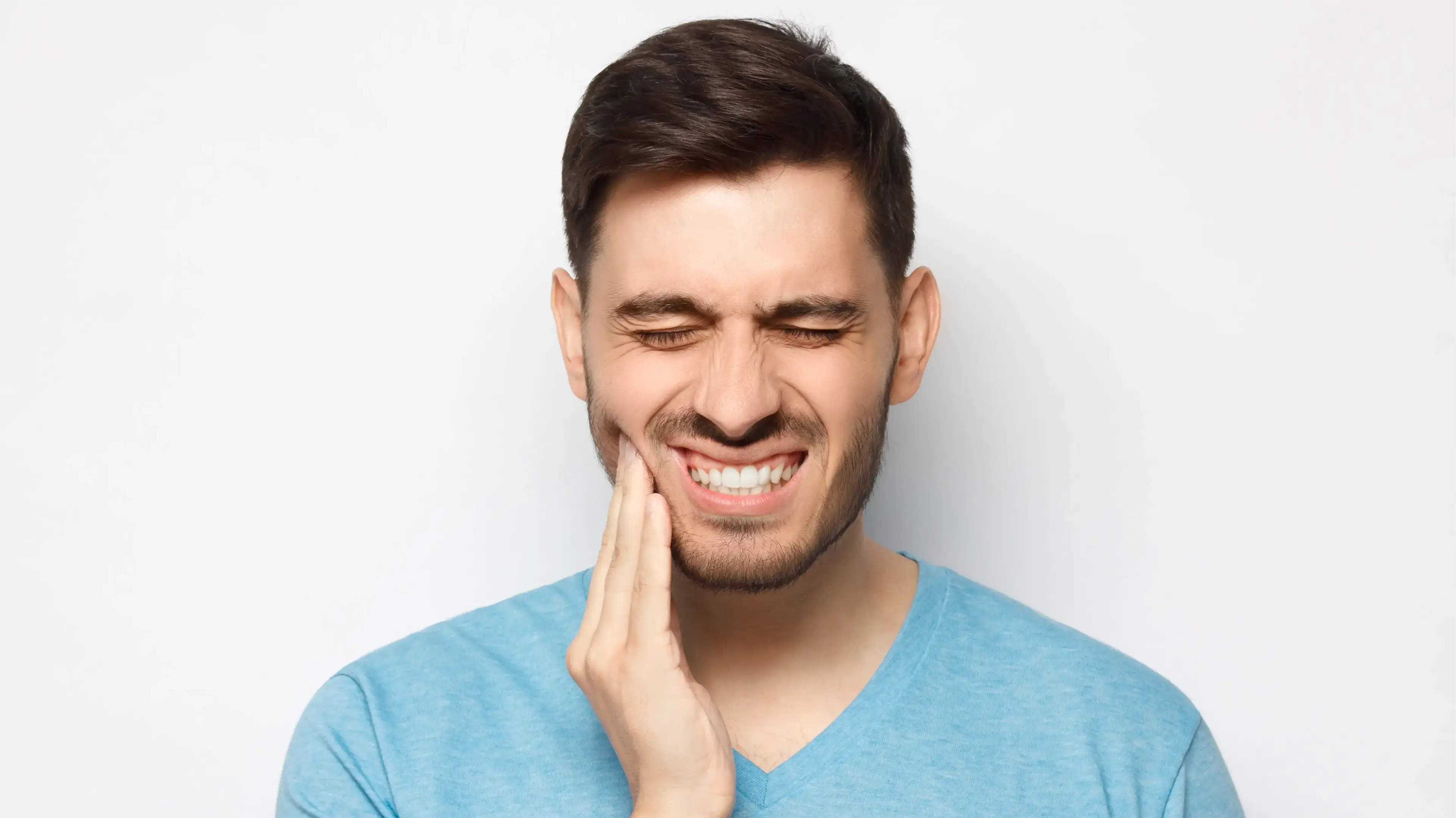 Ein jüngerer Mann, der sich schmerzvoll an seine rechte, untere Kieferseite fasst.