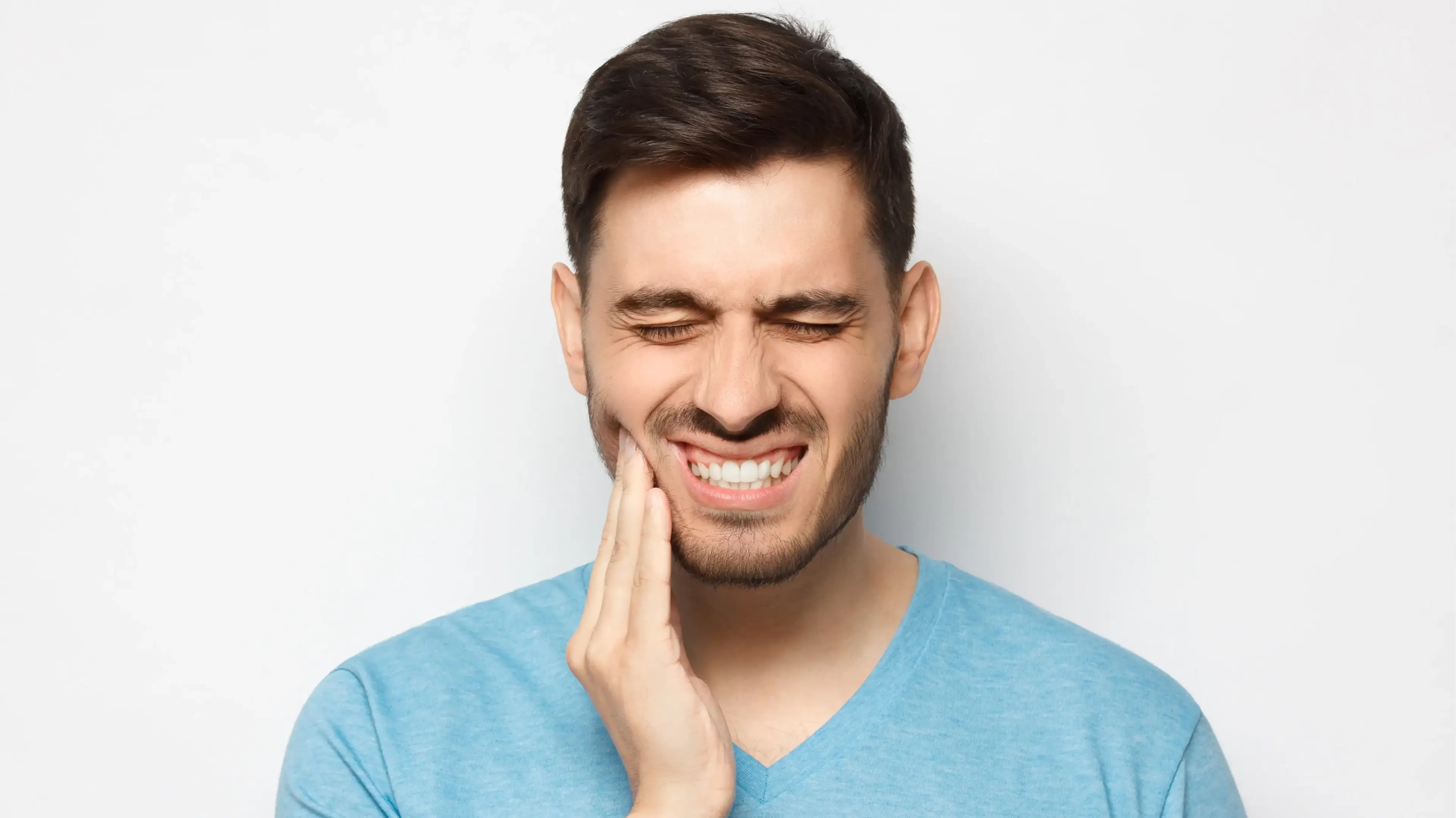 Ein jüngerer Mann, der sich schmerzvoll an seine rechte, untere Kieferseite fasst.