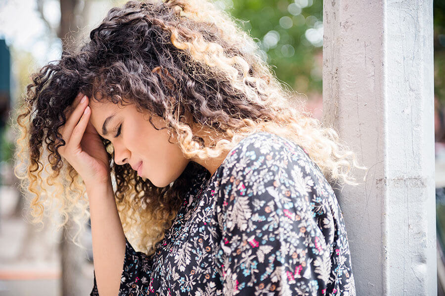 Frau, die sich an den Kopf fasst, wegen Kopfschmerzen als Menstruationsbeschwerden.