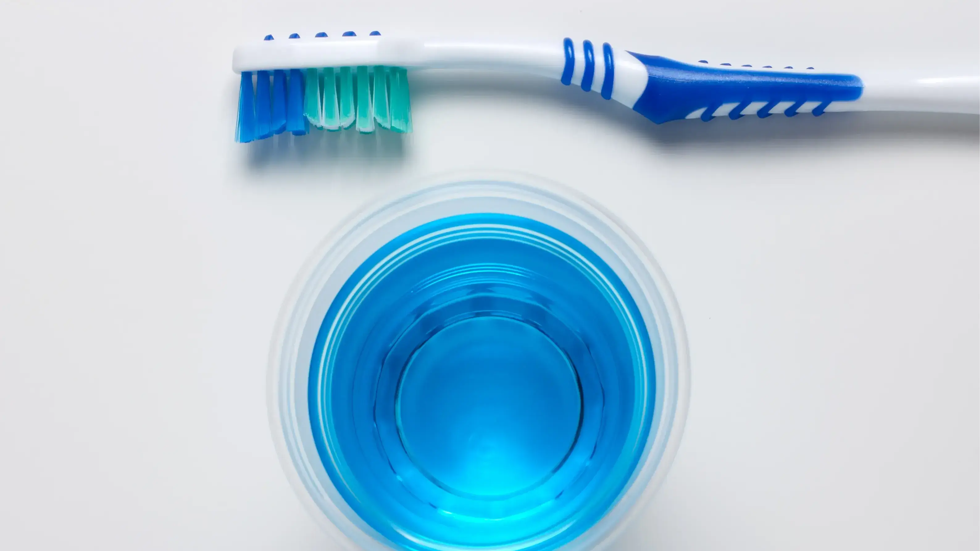 Oben und unten jeweils eine Zahnbürste und in der Mitte ein blaues Mundwasser.