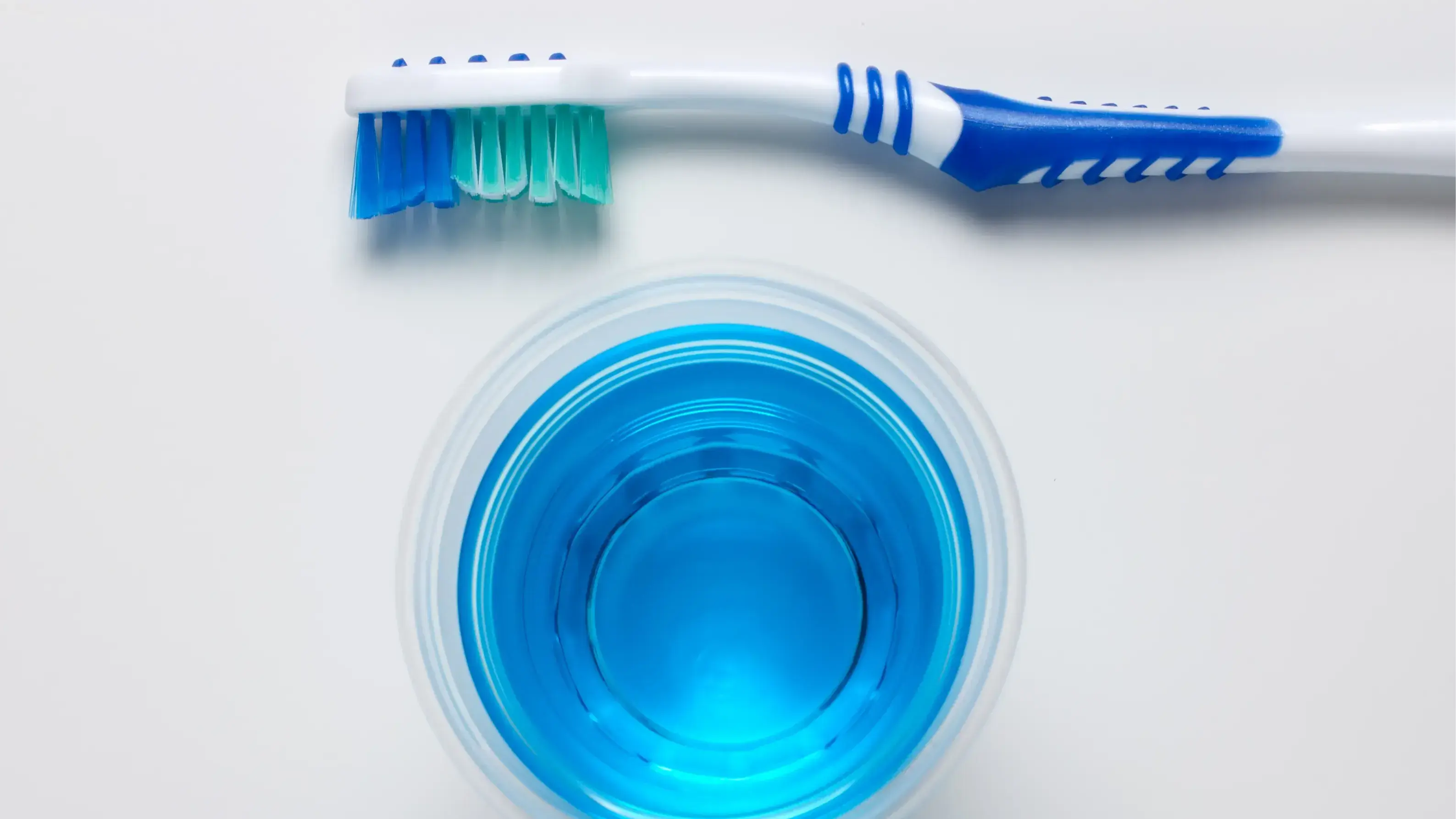 Oben und unten jeweils eine Zahnbürste und in der Mitte ein blaues Mundwasser.