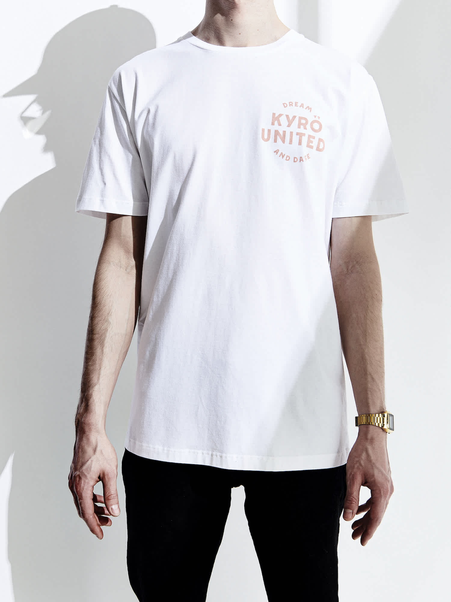 A white, male model wearing a white t-shirt made in collaboration with Kyrö and R-Collection. Pink logo on upper left chest. 
