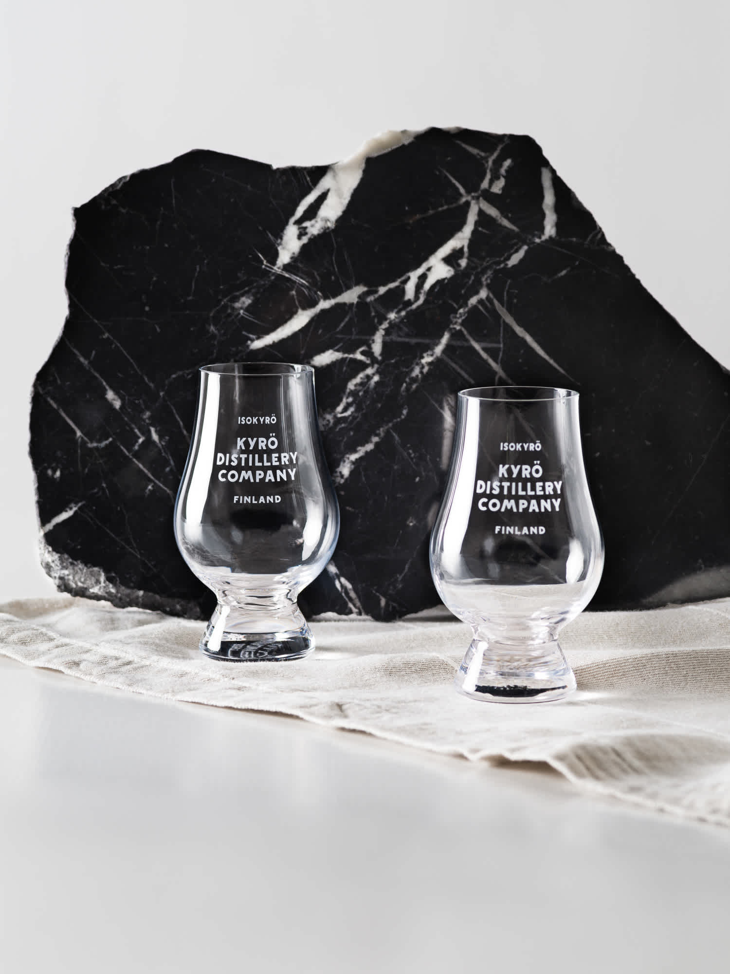 Two clear, Kyrö-branded Glencairn tasting glasses sat on top of natural colored linen and a black slab of granite. 