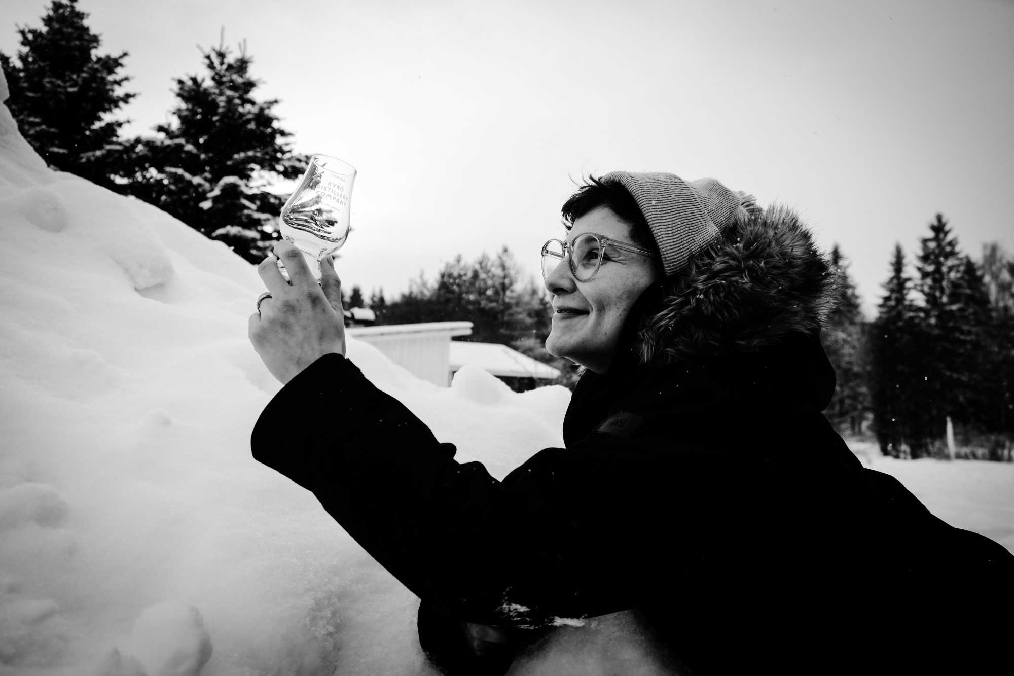 Nainen katsoo hymyillen tyhjää Glencairn-tastinglasia lumisessa maisemassa.