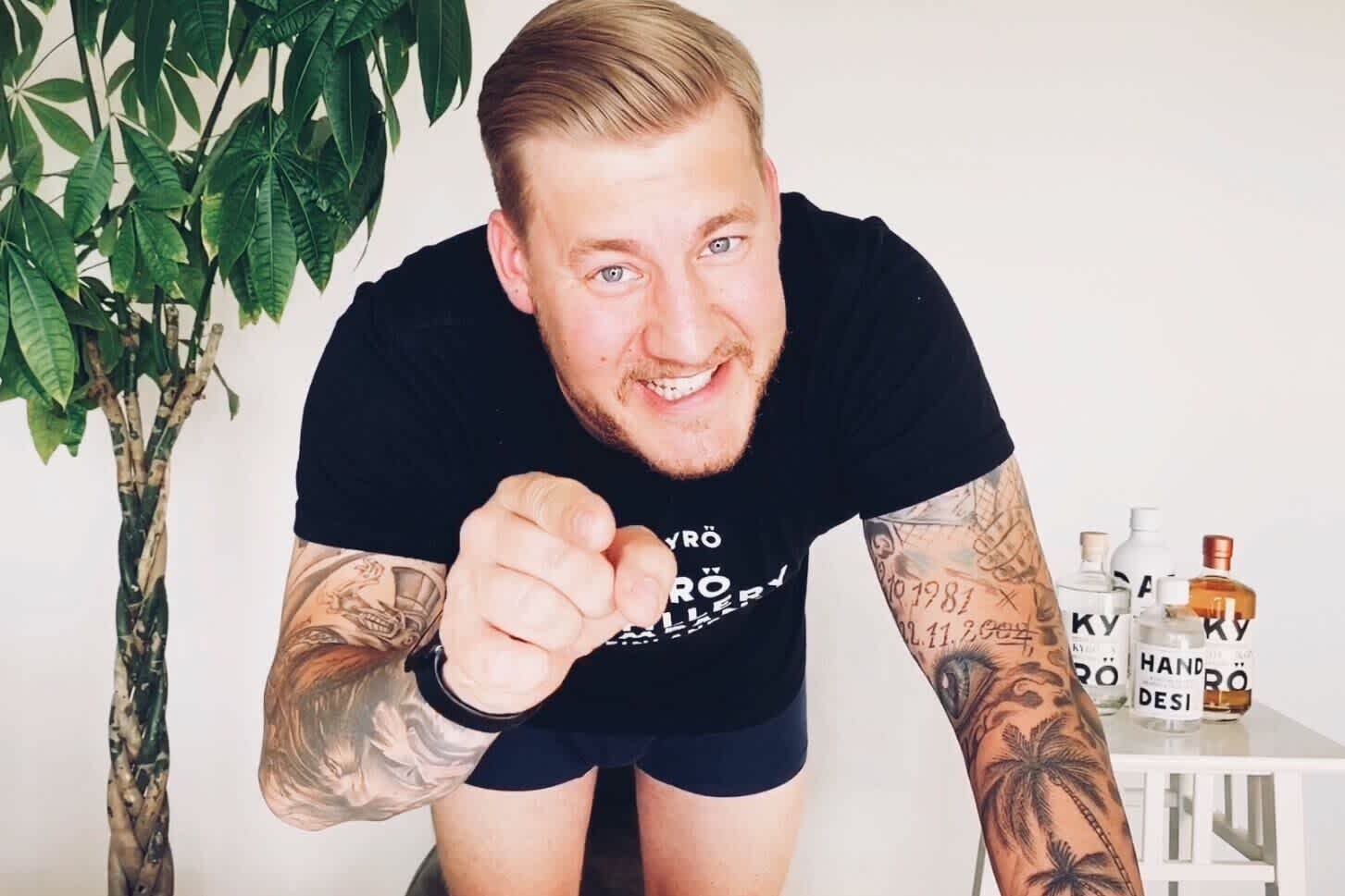 German brand ambassador Max Sabato wearing black underwear and black Kyrö t-shirt pointing at the camera with Kryö bottles standing behind him. 