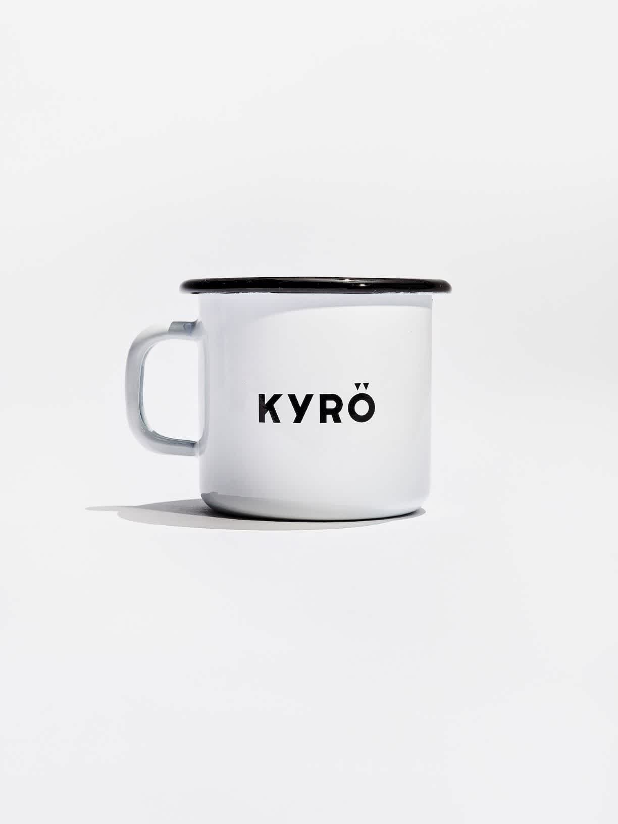 Product photo: a white Muurla enamel mug decorated with a black lip, rye illustration, and Kyrö logo. 