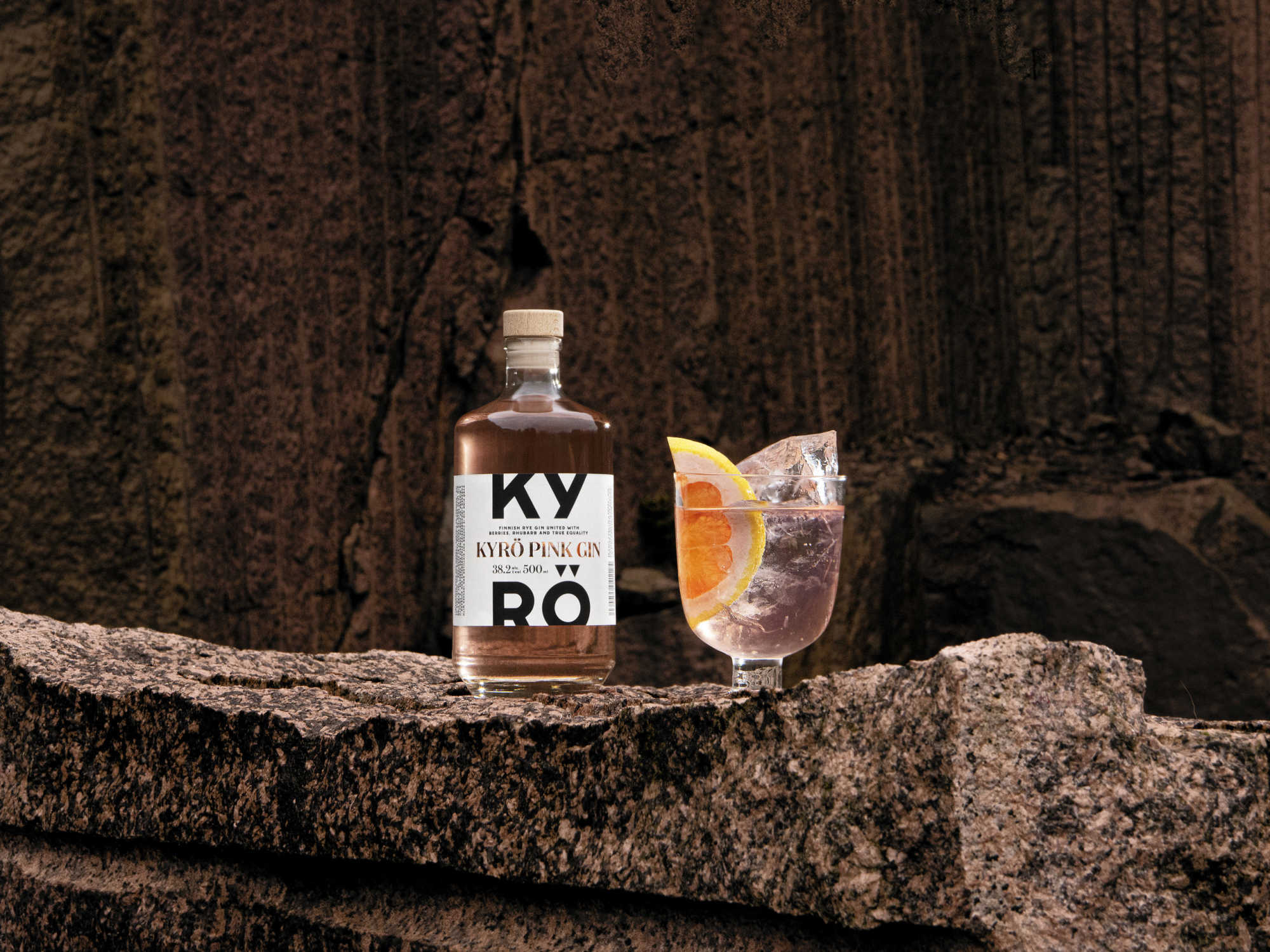 Kyrö Pink Gin 500ml bottle stands on the pink-hued stone next to an Iittala cocktail class filled with soda water, Kyrö Pink Gin, ice, and a slice of pink grapefruit, 