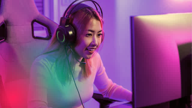 Professional gamer or streamer in a vibrant gaming setup with neon purple and green lighting, wearing headphones while engaging with content. The dynamic lighting creates an immersive esports atmosphere.