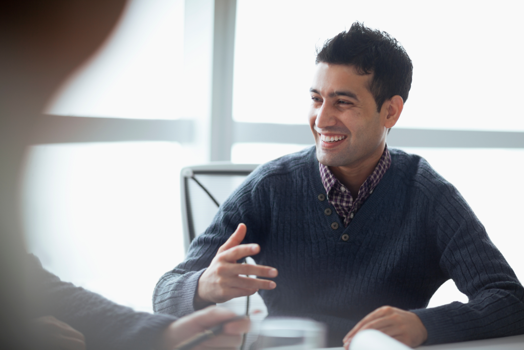 A man in a sweater smiles during a business meeting.