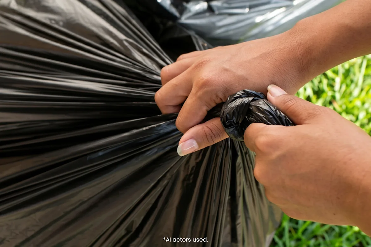 Hands tying a knot in a filled black trash bag to securely seal it for disposal