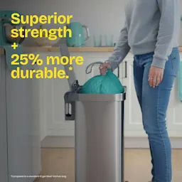A person pulling a teal-color trash bag out of a trash can. The words "Superior strength + 25% more durable." in yellow