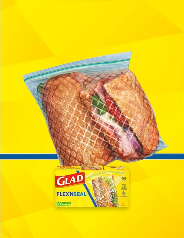 Sandwich in a plastic resealable bag on yellow background with a blue line across. A box of Glad sandwich bags is in front.
