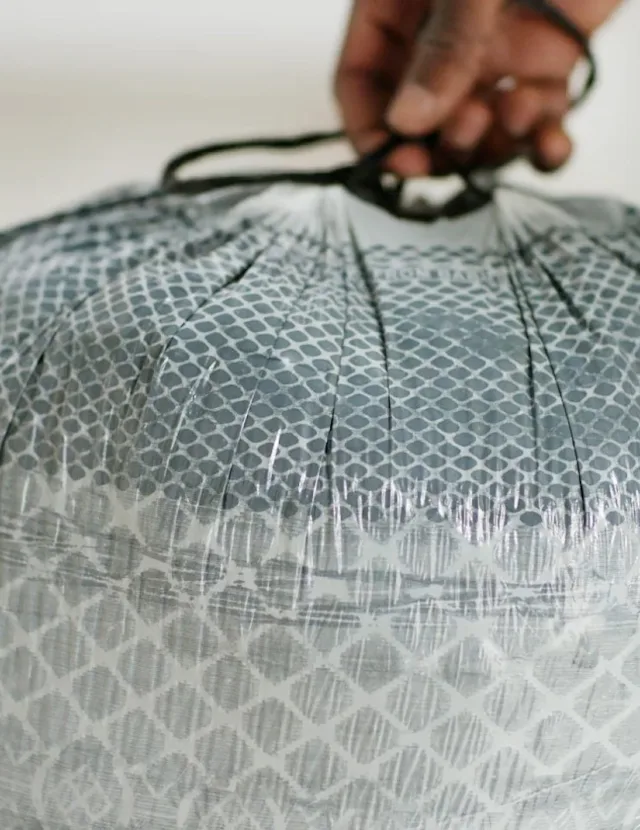 A close-up of a hand holding the drawstring of a gray trash bag