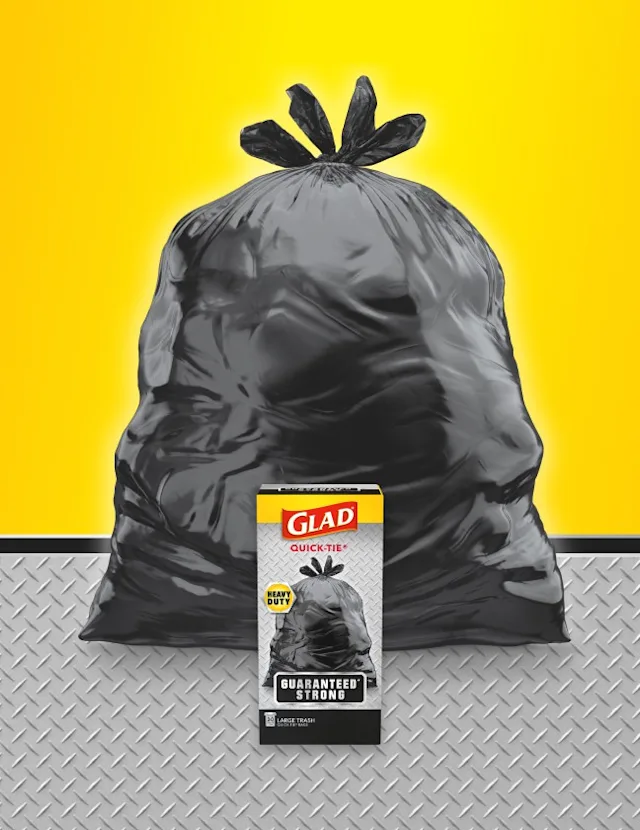 Black trash bag with yellow and metal textured background. Package of Glad trash bags in front.