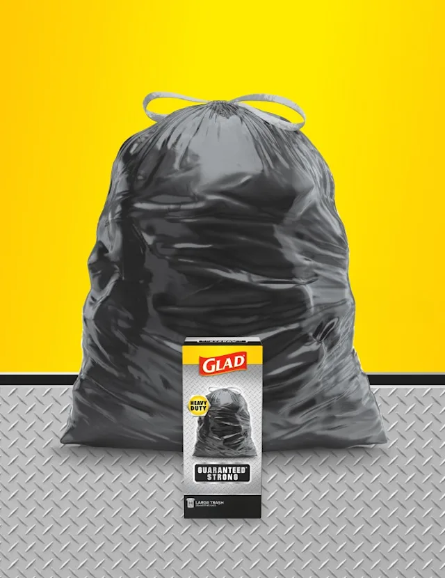 Large black Glad trash bag with yellow drawstrings against a yellow background, with a box of Glad Heavy Duty trash bags in front.