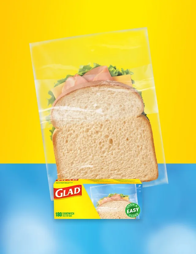Small sandwich in a plastic food bag on a yellow and blue background. A box of Glad sandwich bags is in front.