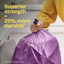 A person pulling a purple trash bag out of a kitchen trash can. The words "Superior strength + 25% more durable." in yellow
