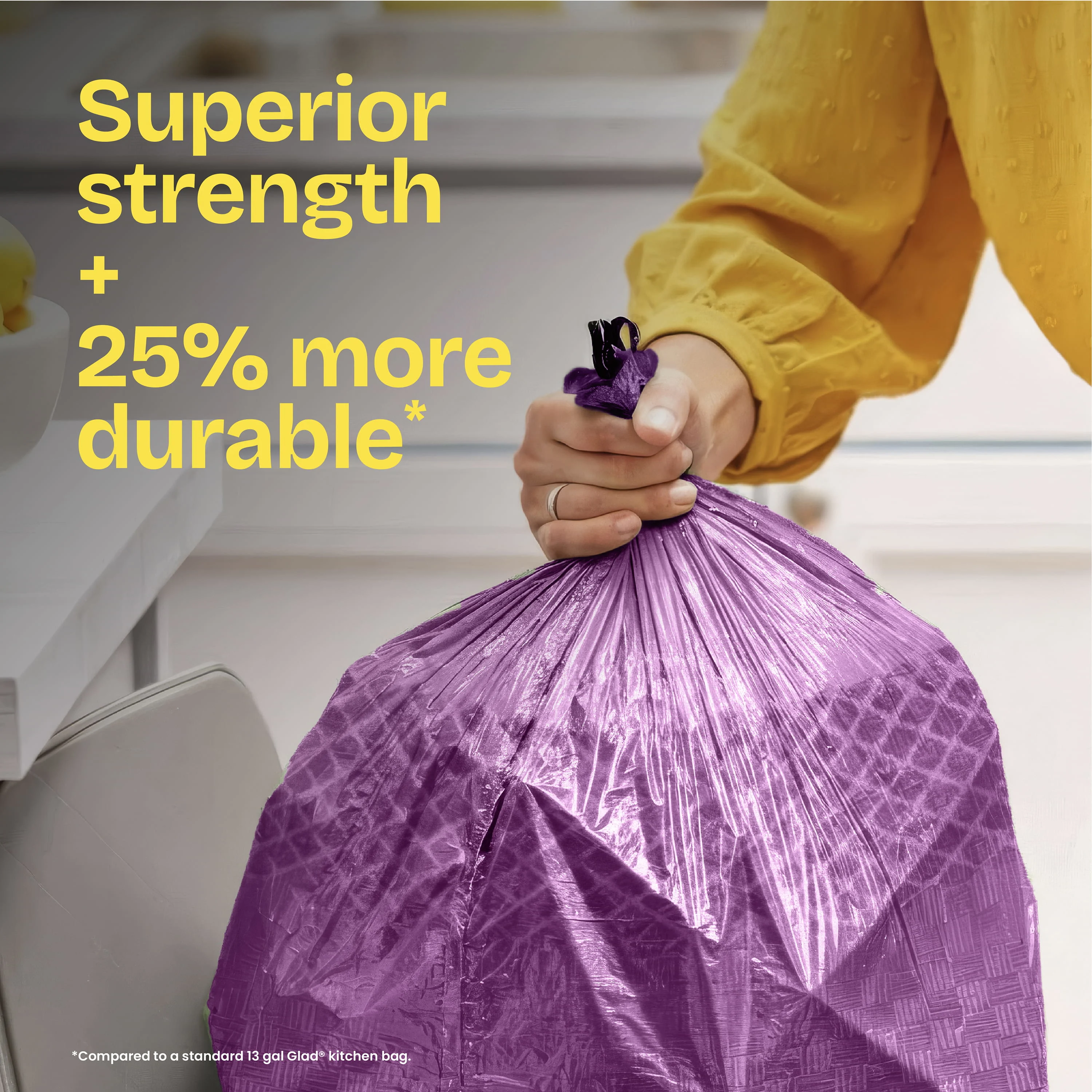 A person pulling a purple trash bag out of a kitchen trash can. The words "Superior strength + 25% more durable." in yellow
