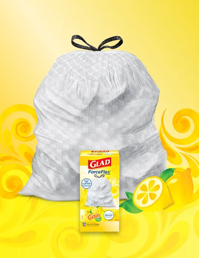 White trashbag with black handles on a background of yellow and with darker yellow swirls and lemons. A box of Glad trash bags sits in front.