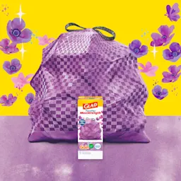 Purple trashbag with black handles on a background of yellow and purple with floral illustrations. A box of Glad trash bags sits in front.