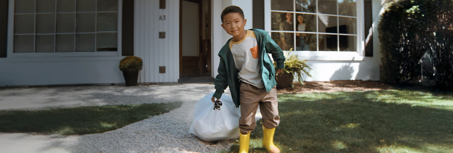 Boy dragging a trash bags in front of a house.