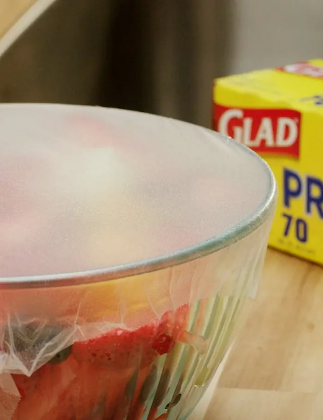 Close-up of a glass bowl covered with plastic wrap. Glad box is in the background.