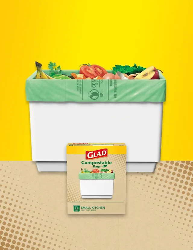 Compost bin with a green bag and vegetable waste on yellow and beige background with box of Glad compostable bags in front.