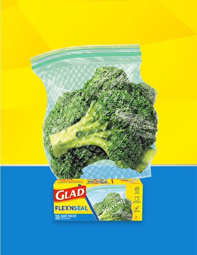 Broccoli florets in a plastic resealable bag on a yellow and blue background. A box of Glad food bags is in front.