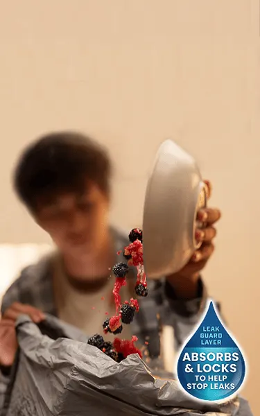 A person pouring berries into a trash bag. A drop shape with the words "Leak Guard layer absorbs & locks to help stop leaks" Glad with LeakGuard absorbs most aqueous liquids.