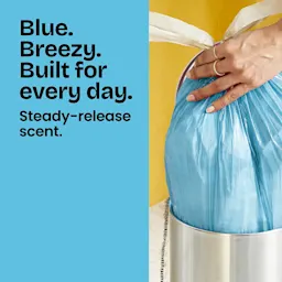 Person putting a blue trash bag in a small trash can. Left panel is blue with the words "Blue. Breezy. Built for every day."