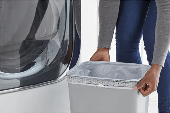 Person in a gray shirt and blue jeans, in a laundry room, putting a fresh trash bag in a medium-sized trash can