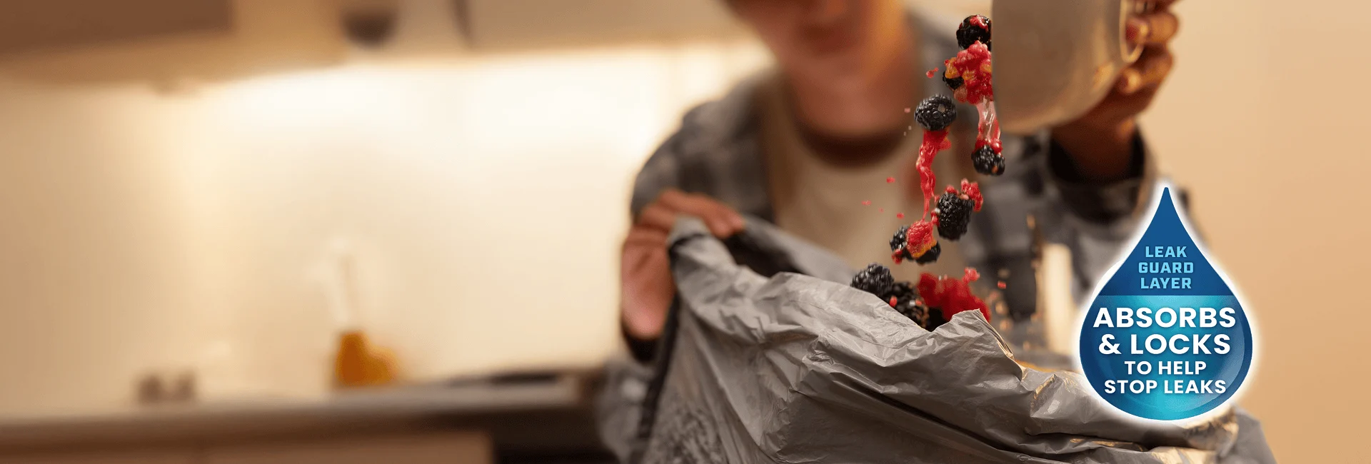 A person pouring berries into a trash bag. A drop shape with the words "Leak Guard layer absorbs & locks to help stop leaks" Glad with LeakGuard absorbs most aqueous liquids.