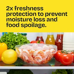 A glass bowl of shrimp covered with Cling'n Seal on a refrigerator shelf. The words "2X freshness protection prevents moisture loss & food spoilage"