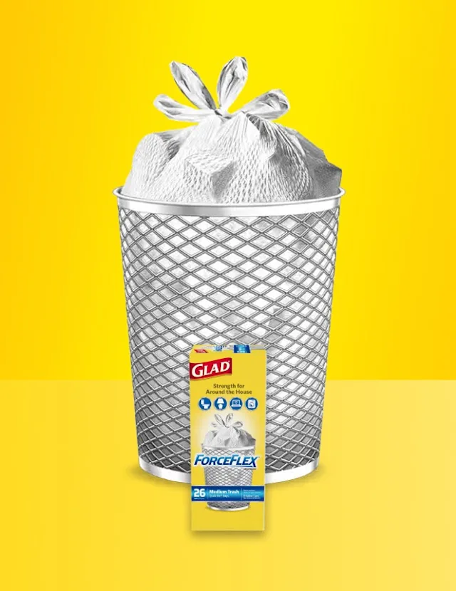 Glad ForceFlex trash bag in a silver mesh trash can against a yellow background with product packaging in front.